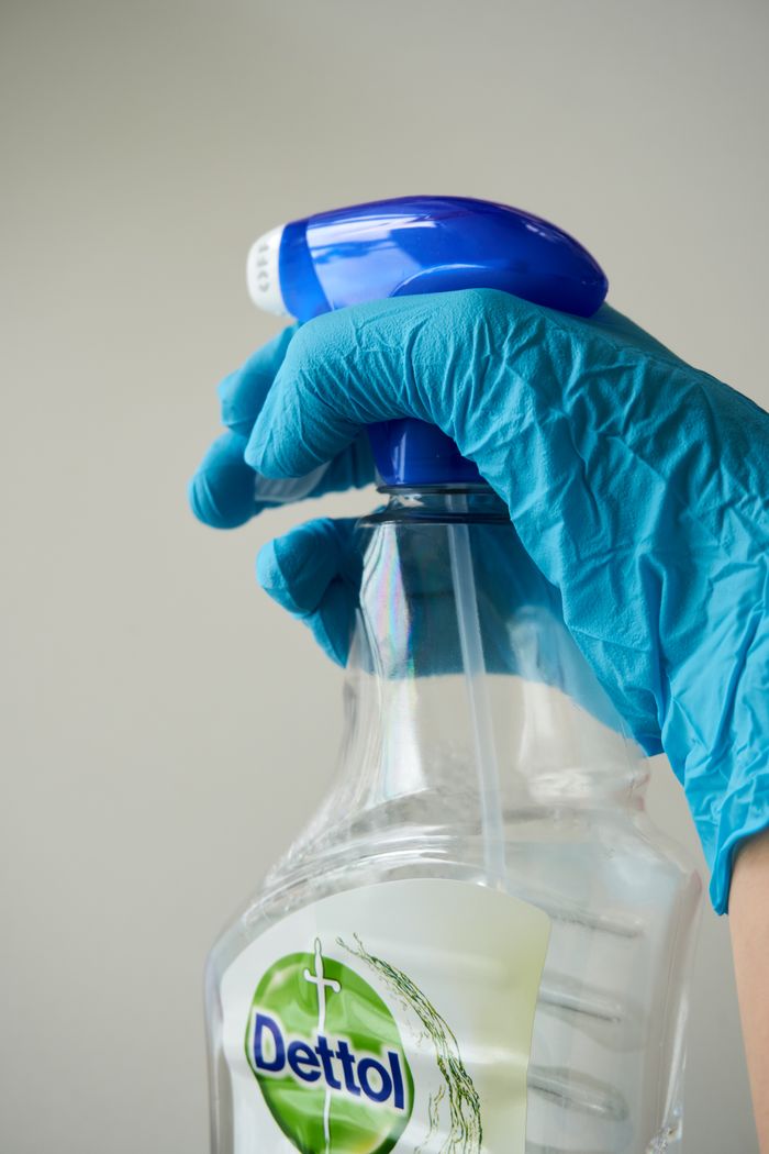 Close-up of a blue-gloved hand holding a cleaning spray bottle indoors.